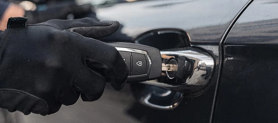 Hand mit schwarzem Handschuh steckt Autoschlüssel in Türgriff eines schwarzen Autos.