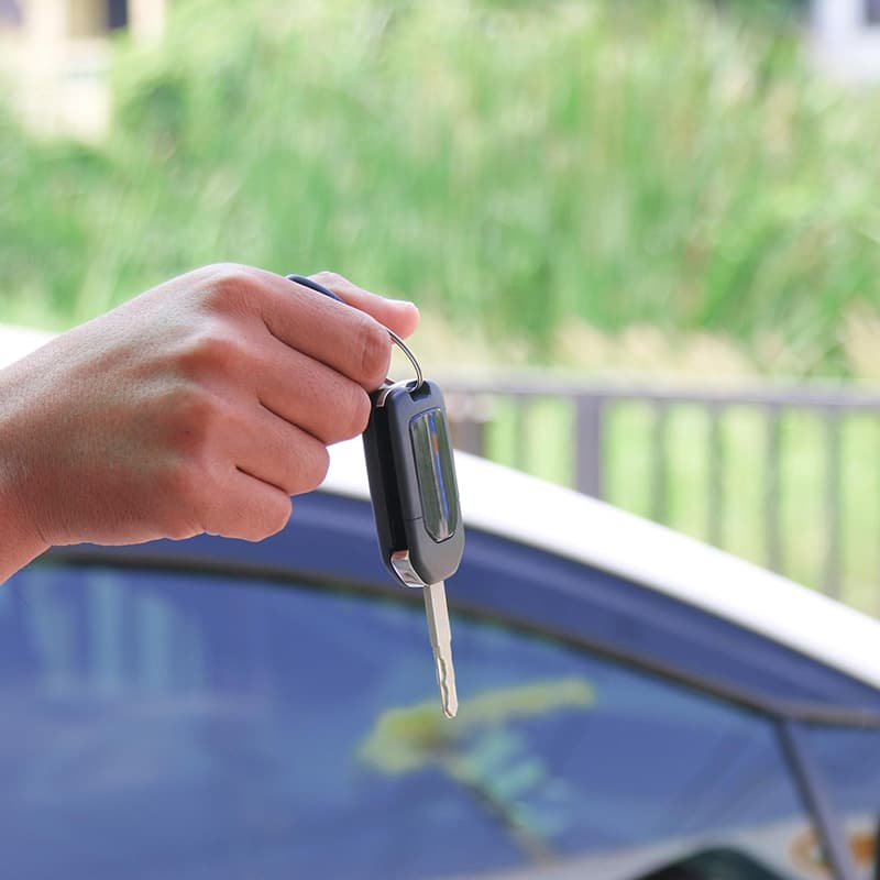 Hand hält einen Autoschlüssel neben einem geparkten Auto