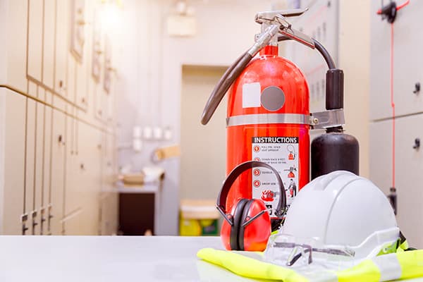 Feuerlöscher, Schutzhelm und Warnweste auf einem Tisch