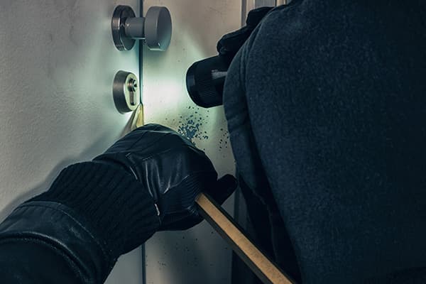 Behandschuhte Hand setzt ein Werkzeug am Schließzylinder einer Tür an