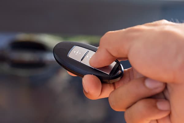 Hand drückt die Taste eines Funkschlüssels vor einem Auto