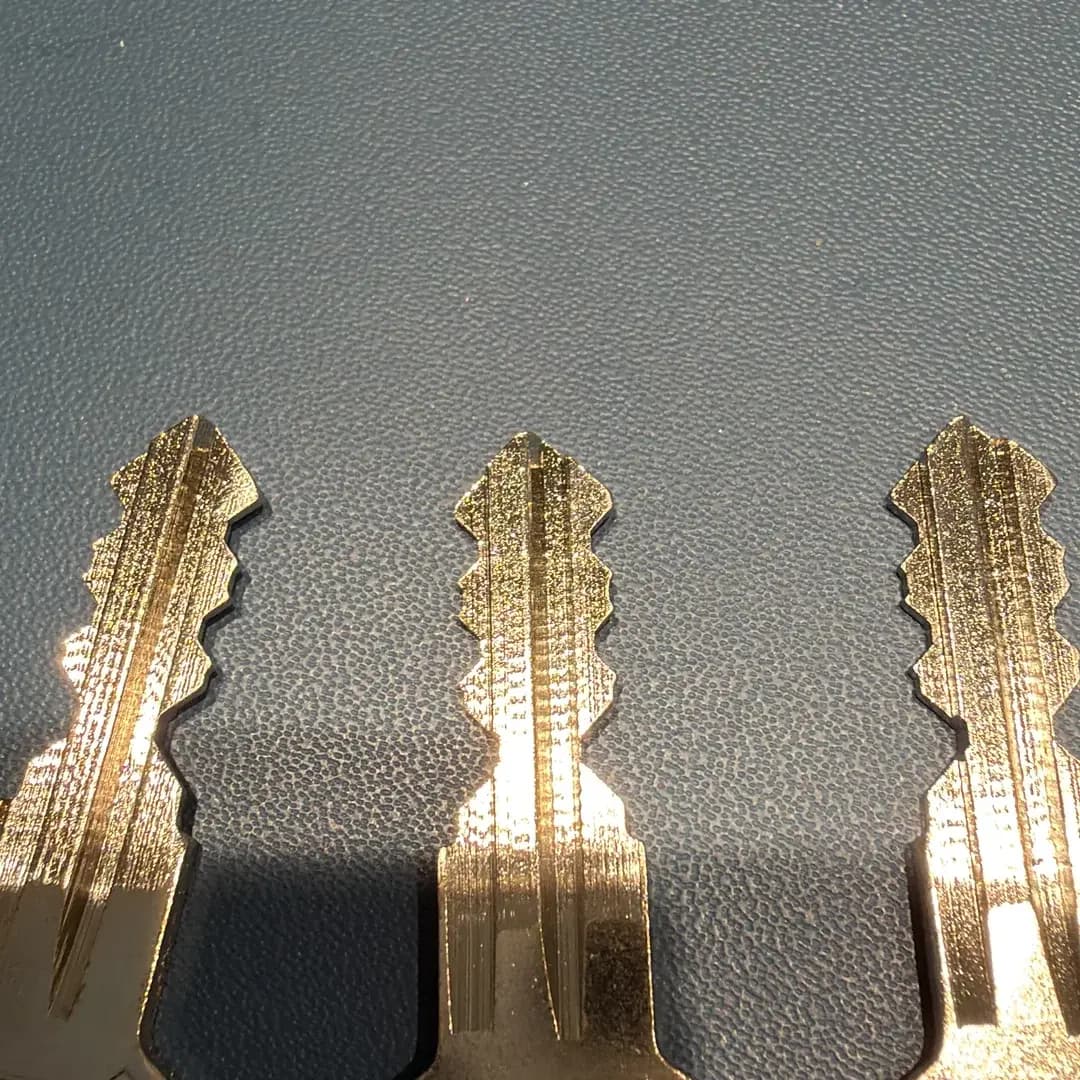 Drei goldene Schlüssel liegen nebeneinander auf einer dunklen, strukturierten Oberfläche.