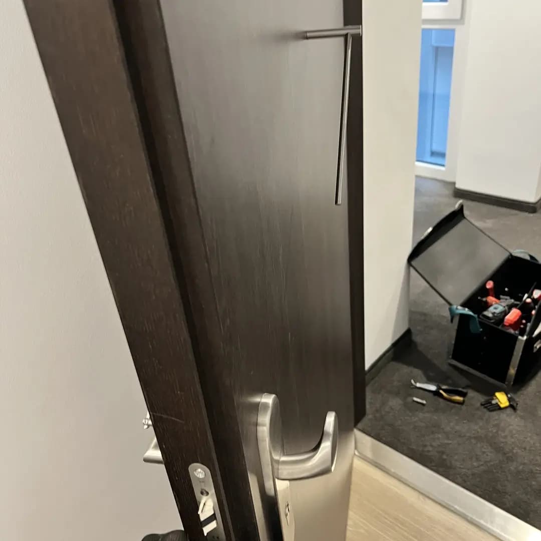 Geöffnete Holztür mit Metallgriff und Werkzeugkasten mit Werkzeugen auf dunklem Teppichboden.