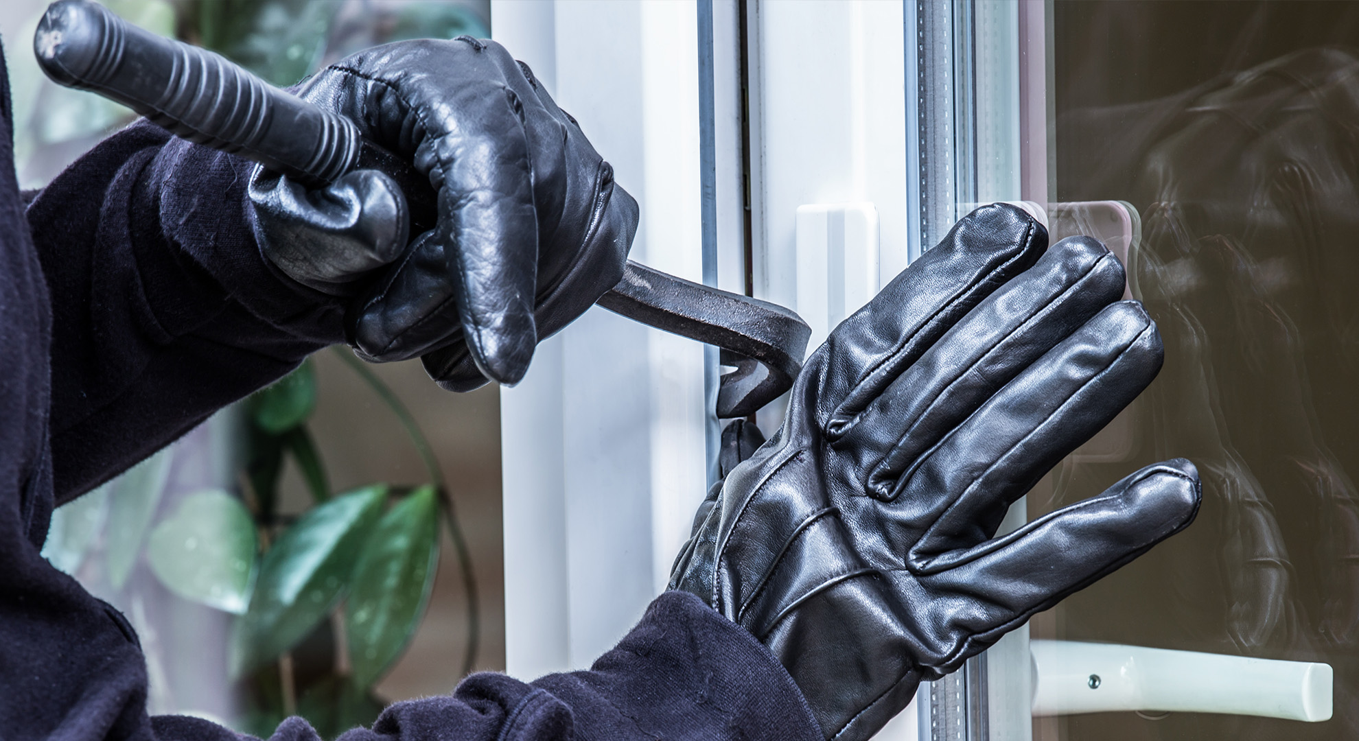 Behandschuhte Hände hebeln ein Fenster mit einem Brecheisen auf