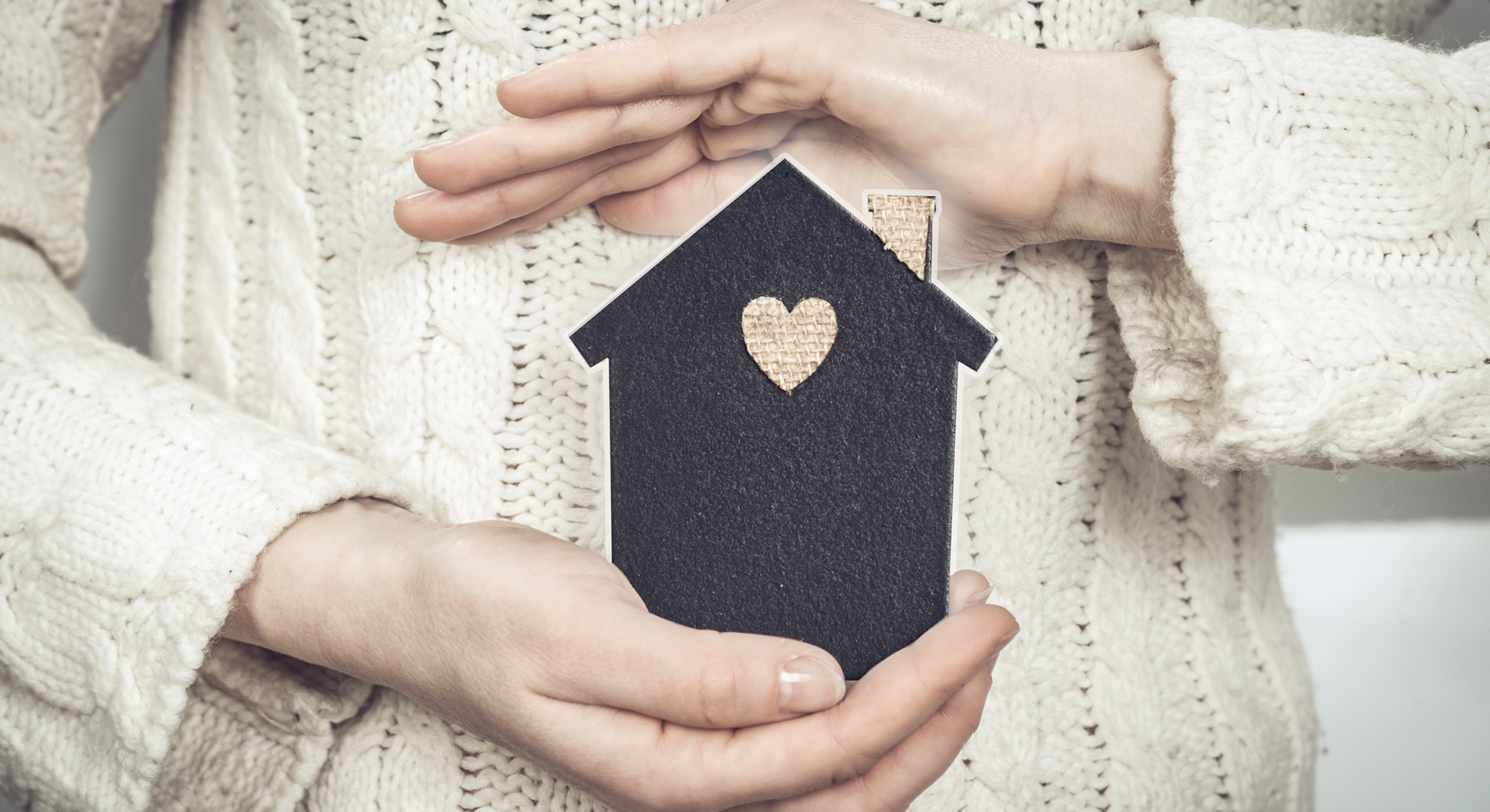 Hände halten schützend ein Haus-Symbol aus Filz